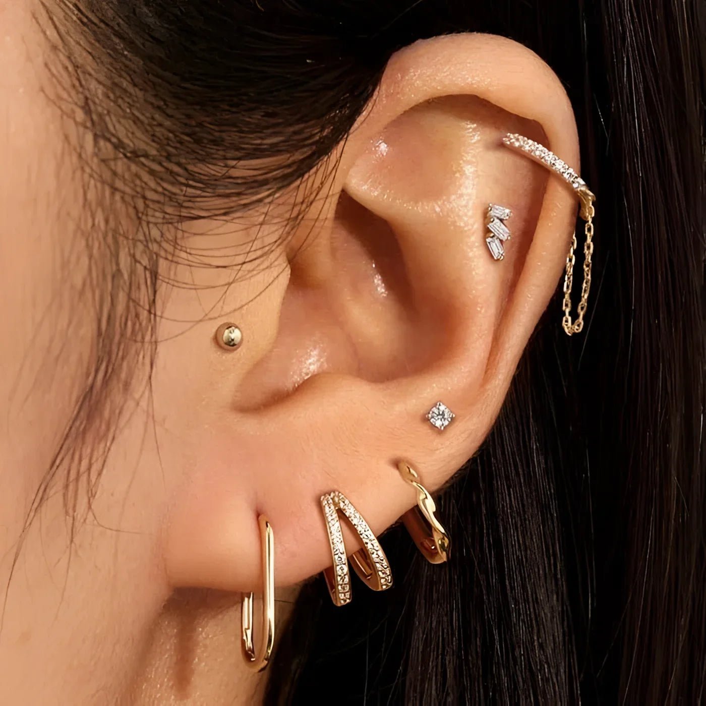 Ear with multiple gold and jeweled piercings wearing 14K Gold Essential Oval Huggie Hoops