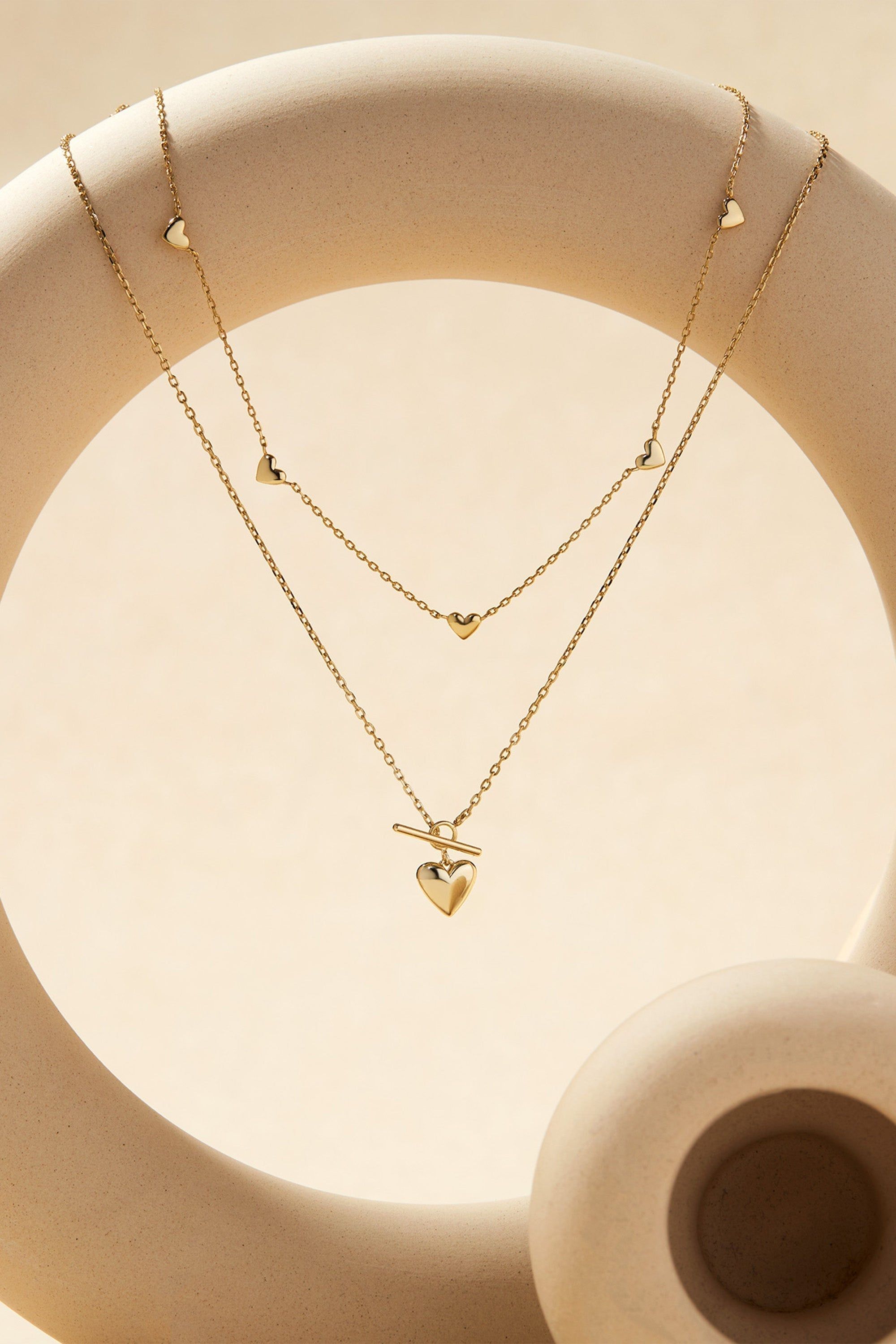 Two layered gold necklaces with heart-shaped charms from the Micro Heart Toggle Pendant Necklace collection