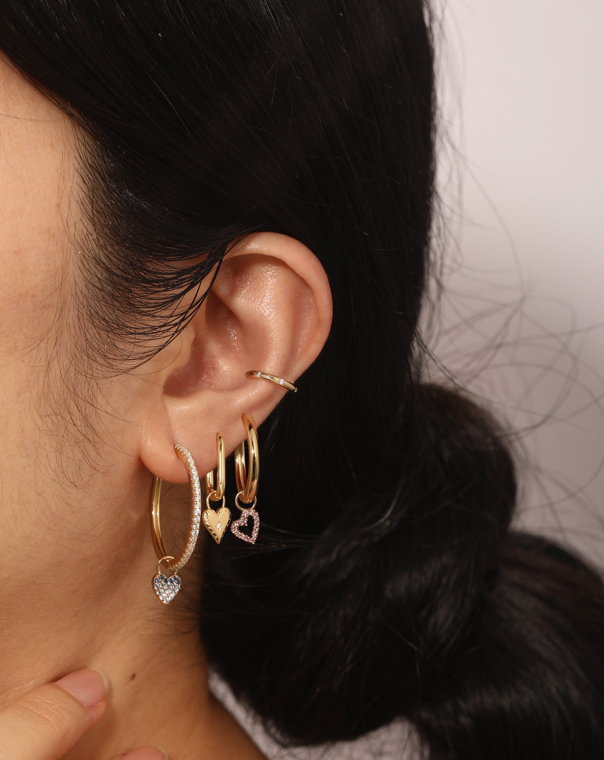 Ear with gold hoop earrings and cuff wearing the Open Heart Hoop Charm jewelry piece