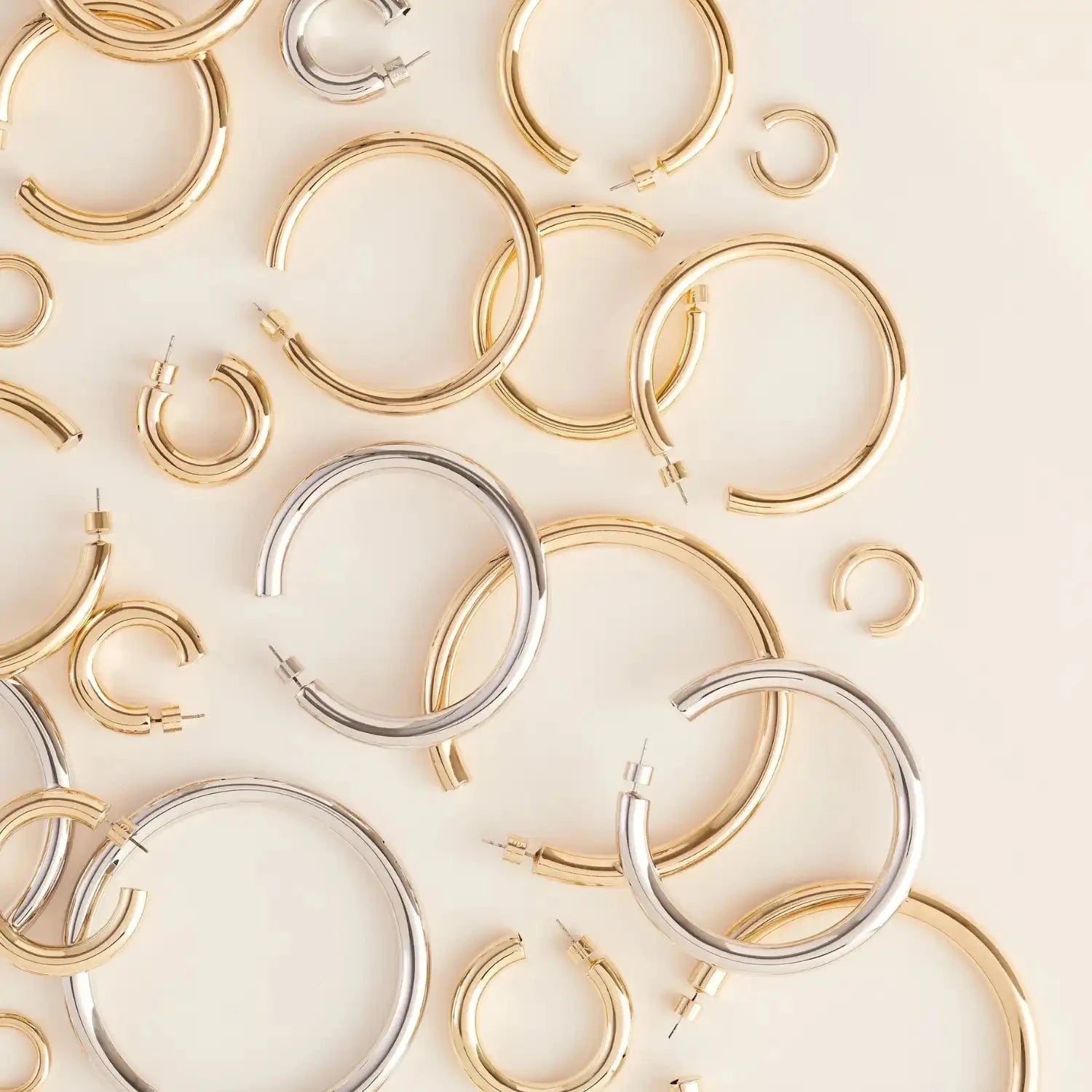 Collection of gold and silver hoop earrings on a light beige background