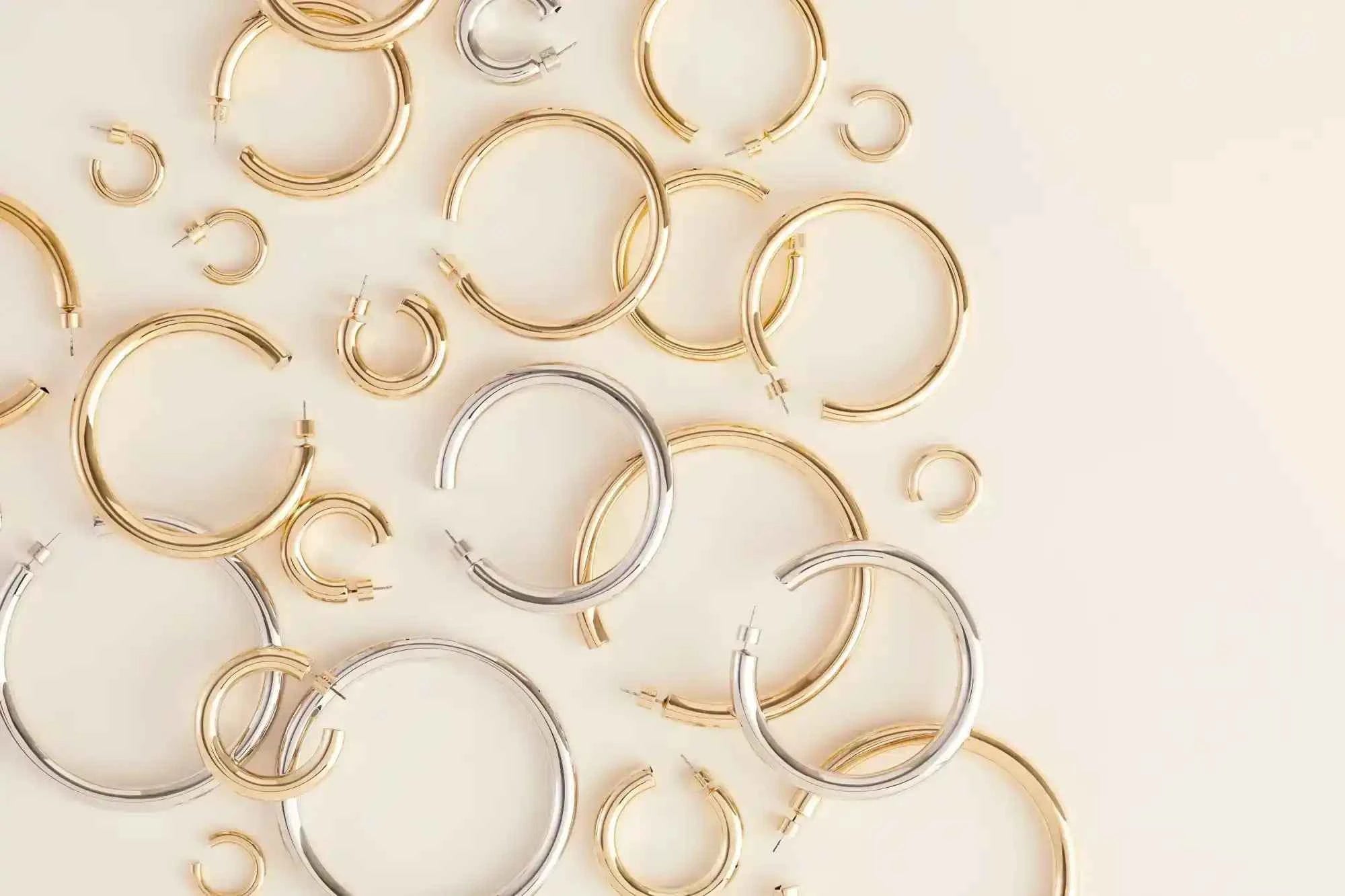 Collection of gold and silver hoop earrings on a light beige background