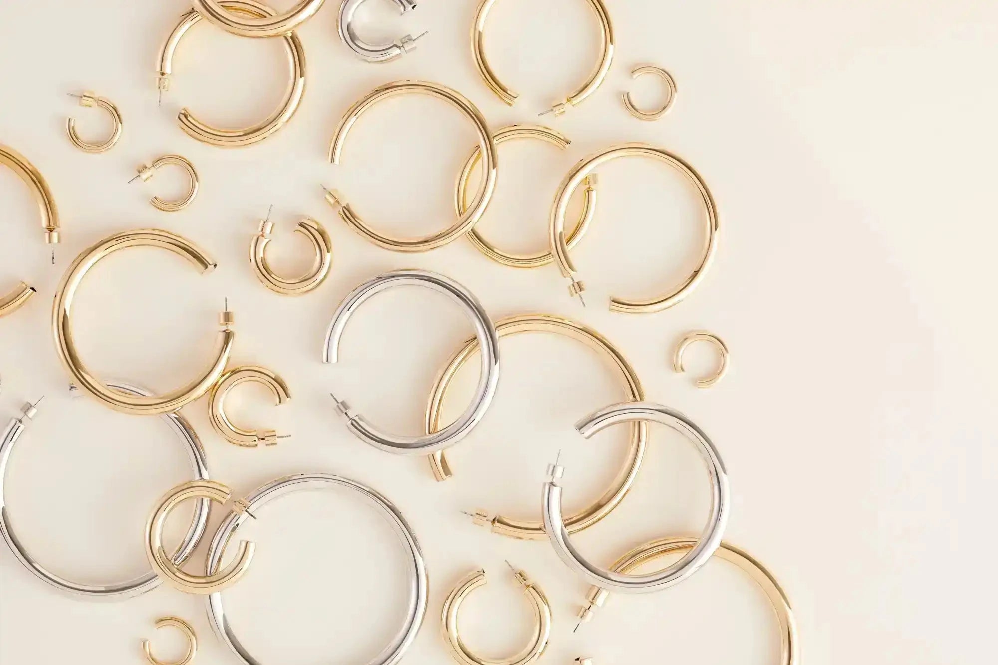 Collection of gold and silver hoop earrings on a light beige background
