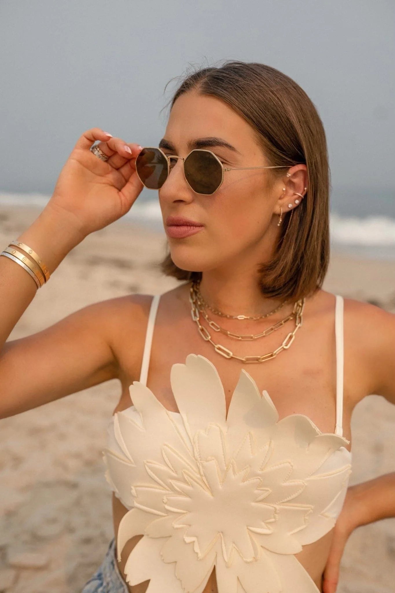 Woman wearing sunglasses and floral top showcasing the Dr Bridget Necklace in brass plated 14k gold