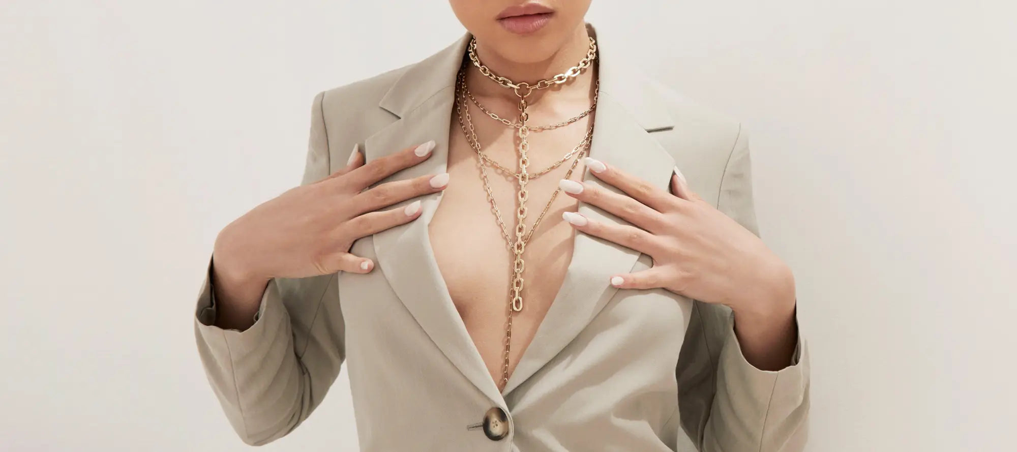 Woman in a beige blazer showcasing layered gold necklaces from the Lariat Necklaces collection
