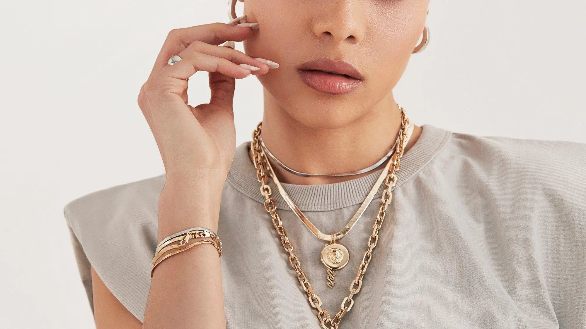 Woman modeling layered gold necklaces and bracelets in New Arrivals jewelry collection