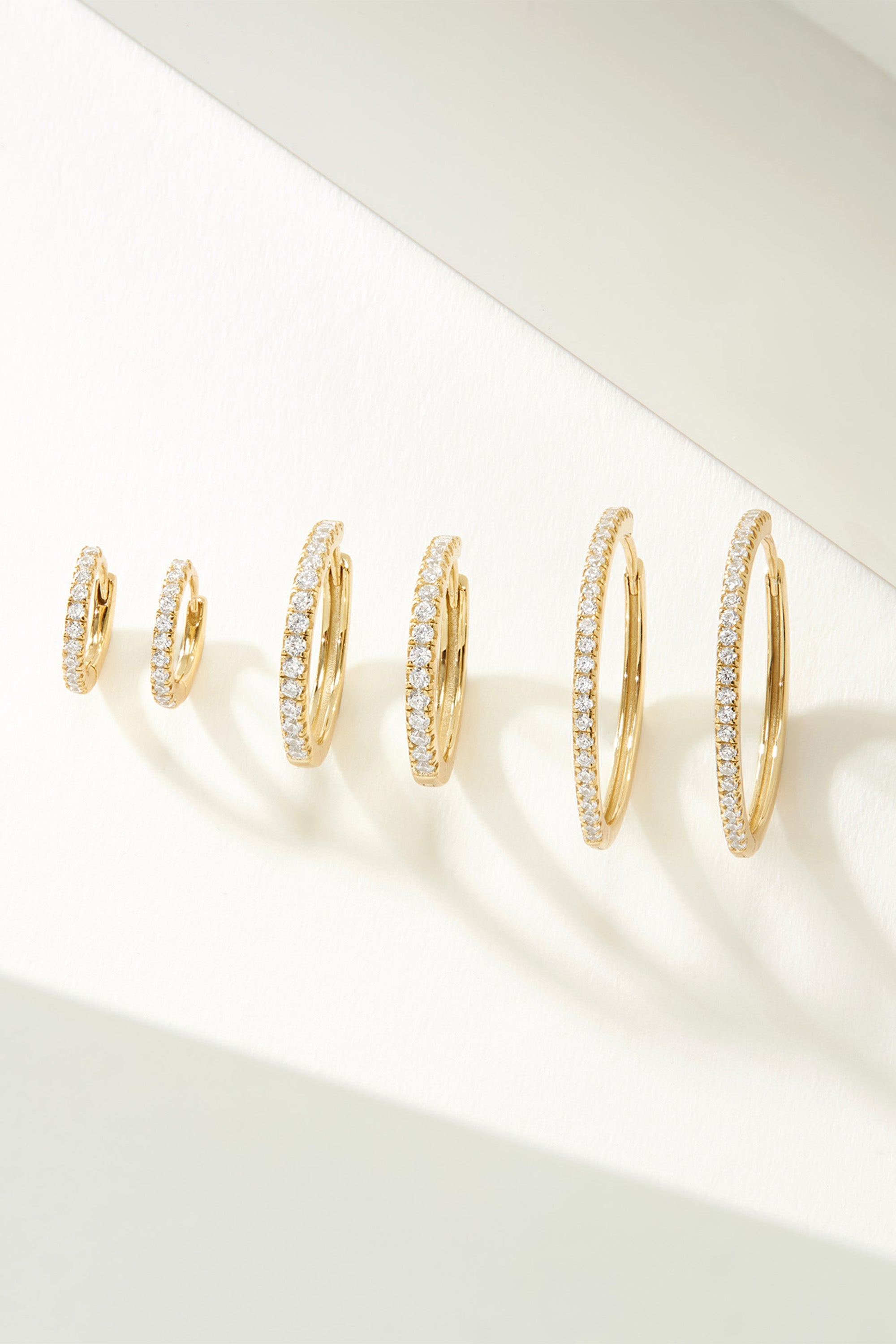 Six pairs of gold diamond-encrusted Mini CZ Huggie Hoop Earrings displayed elegantly