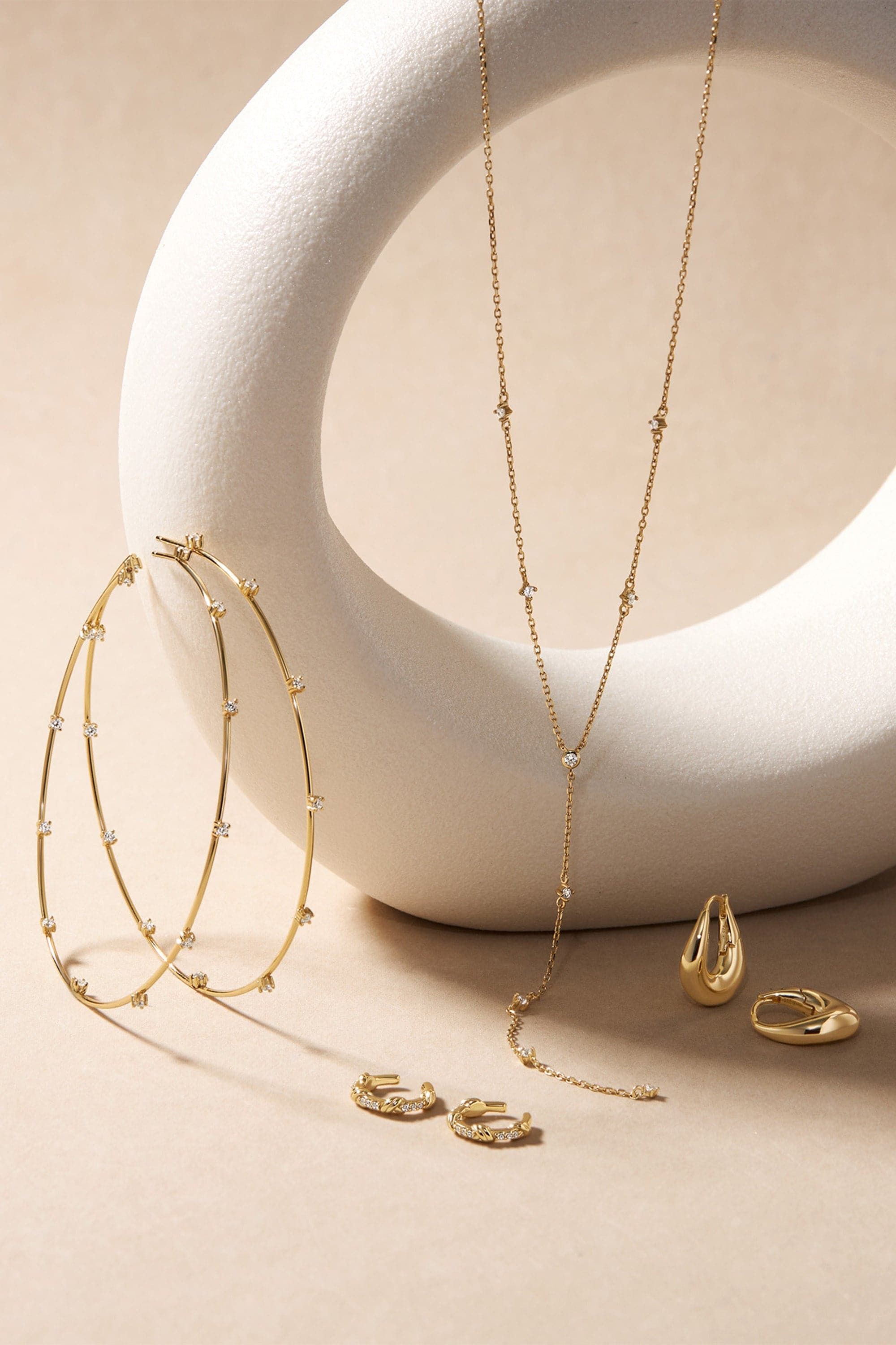 Gold jewelry collection with diamond accents including hoop earrings, lariat necklace, and rings