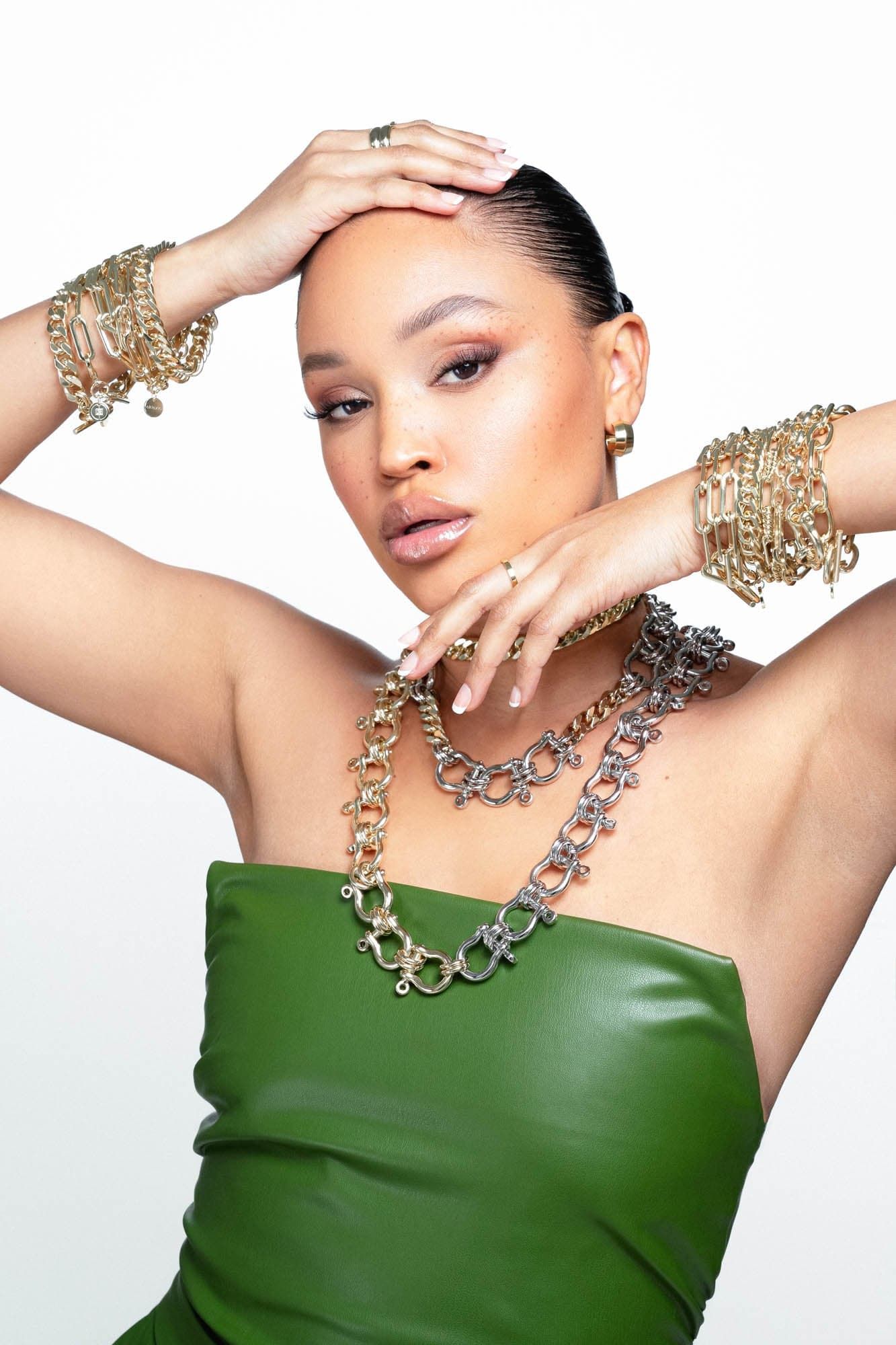 Woman in a green top showing off the Enzo Bracelet with shiny gold jewelry