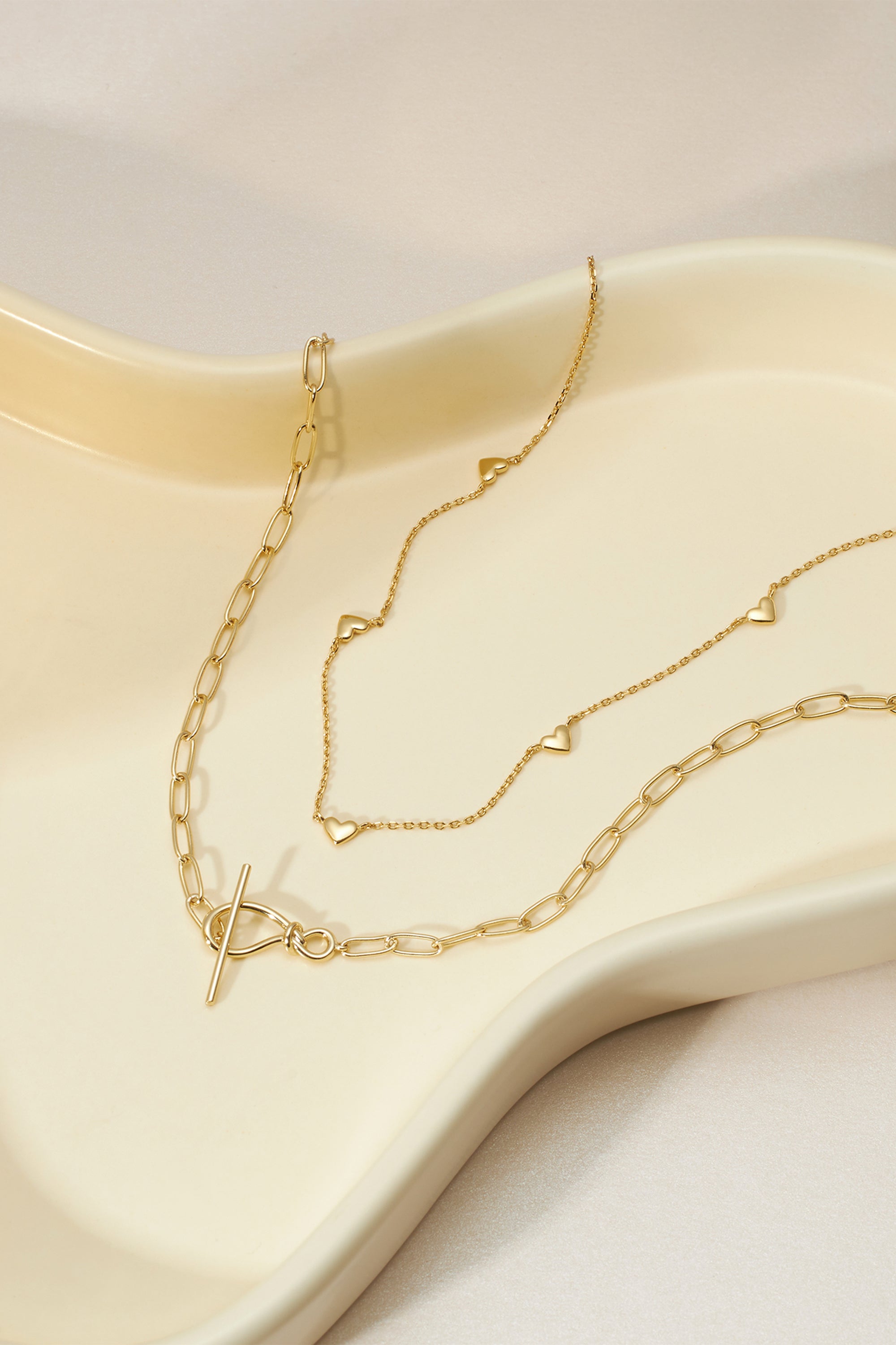 Two gold necklaces featuring knot toggle and paperclip chain styles