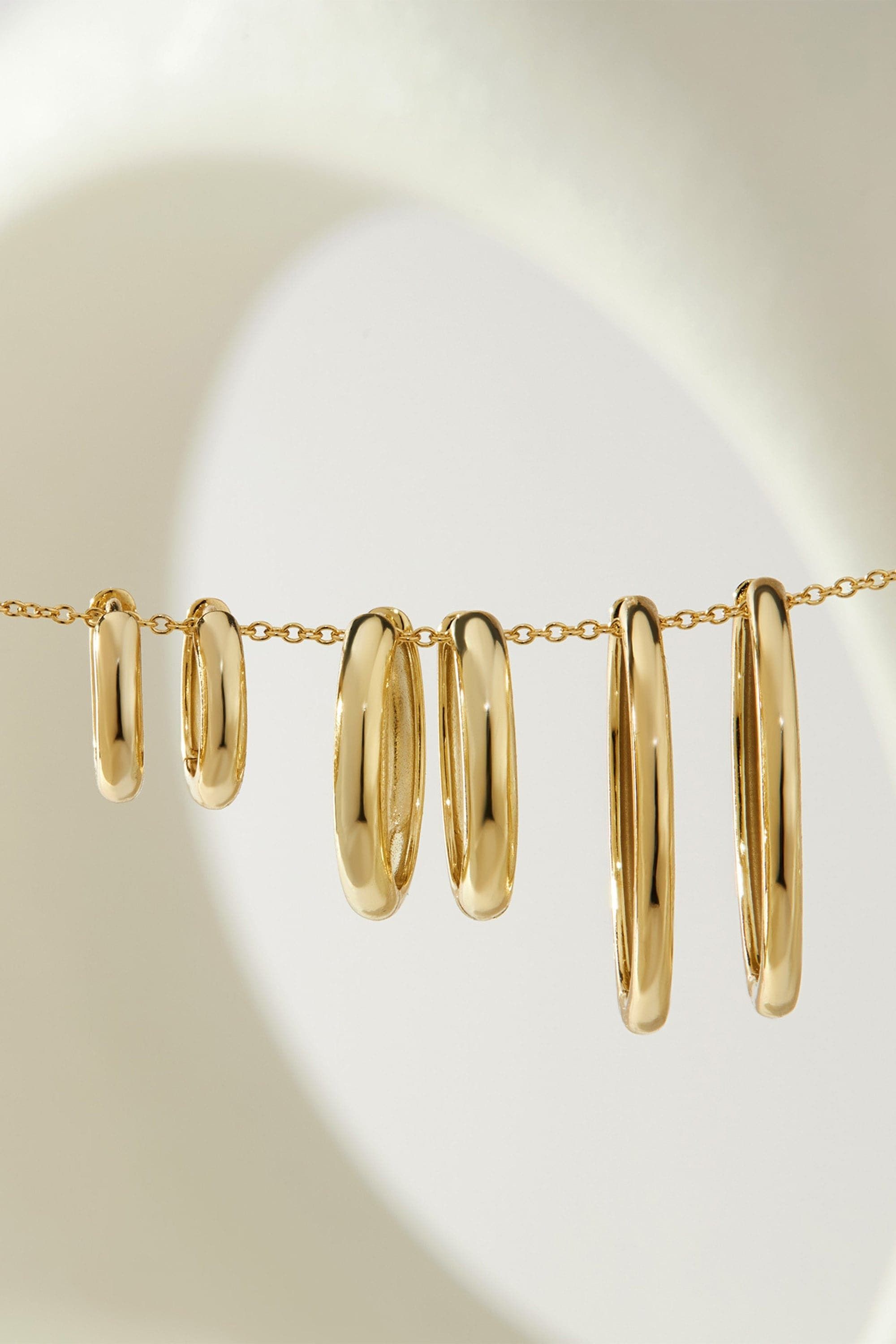 Gold hoop earrings on a chain from Mini Huggie Hoop Earrings collection