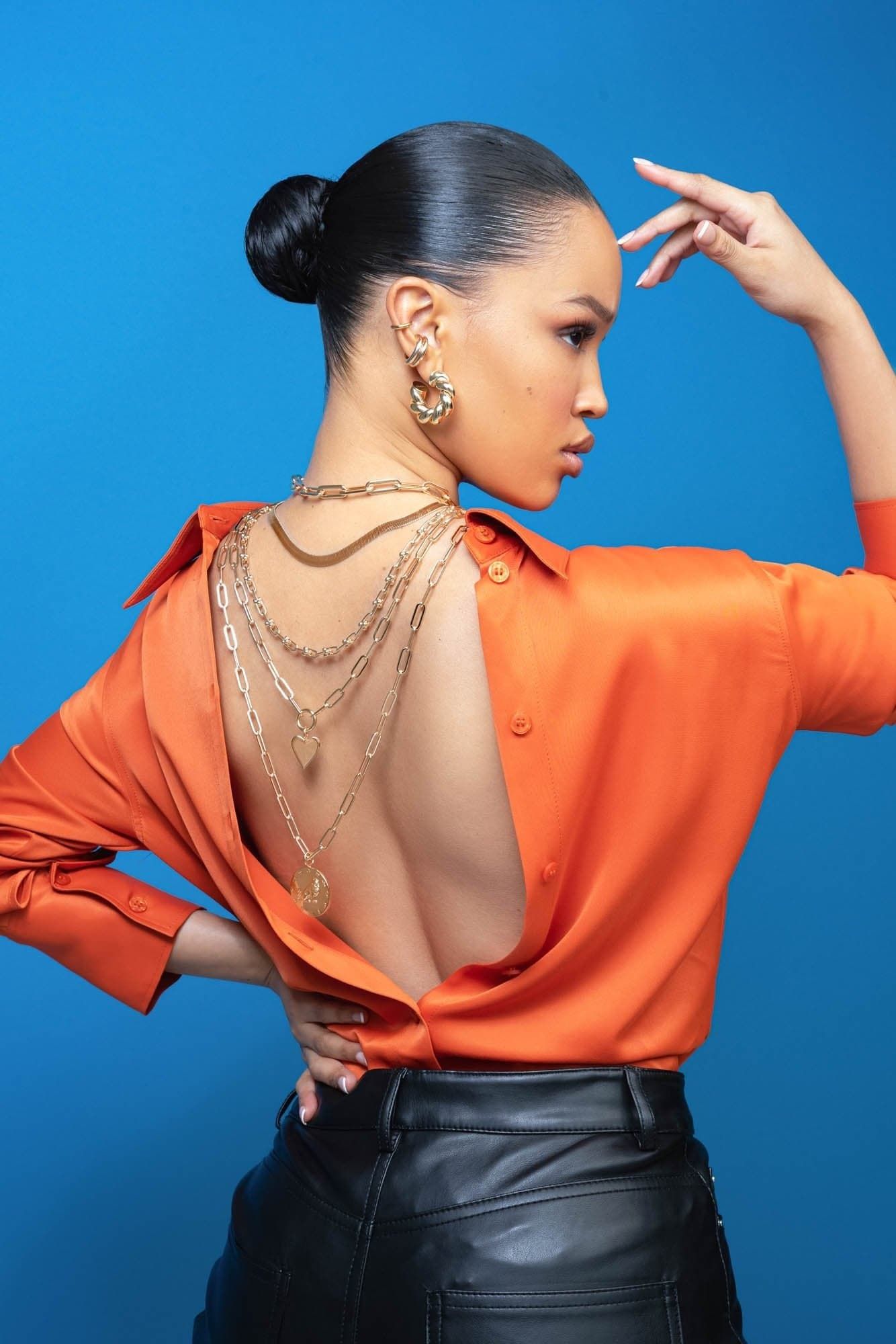 Woman in open-back orange shirt with layered gold necklaces wearing Zodiac Pendant Capricorn