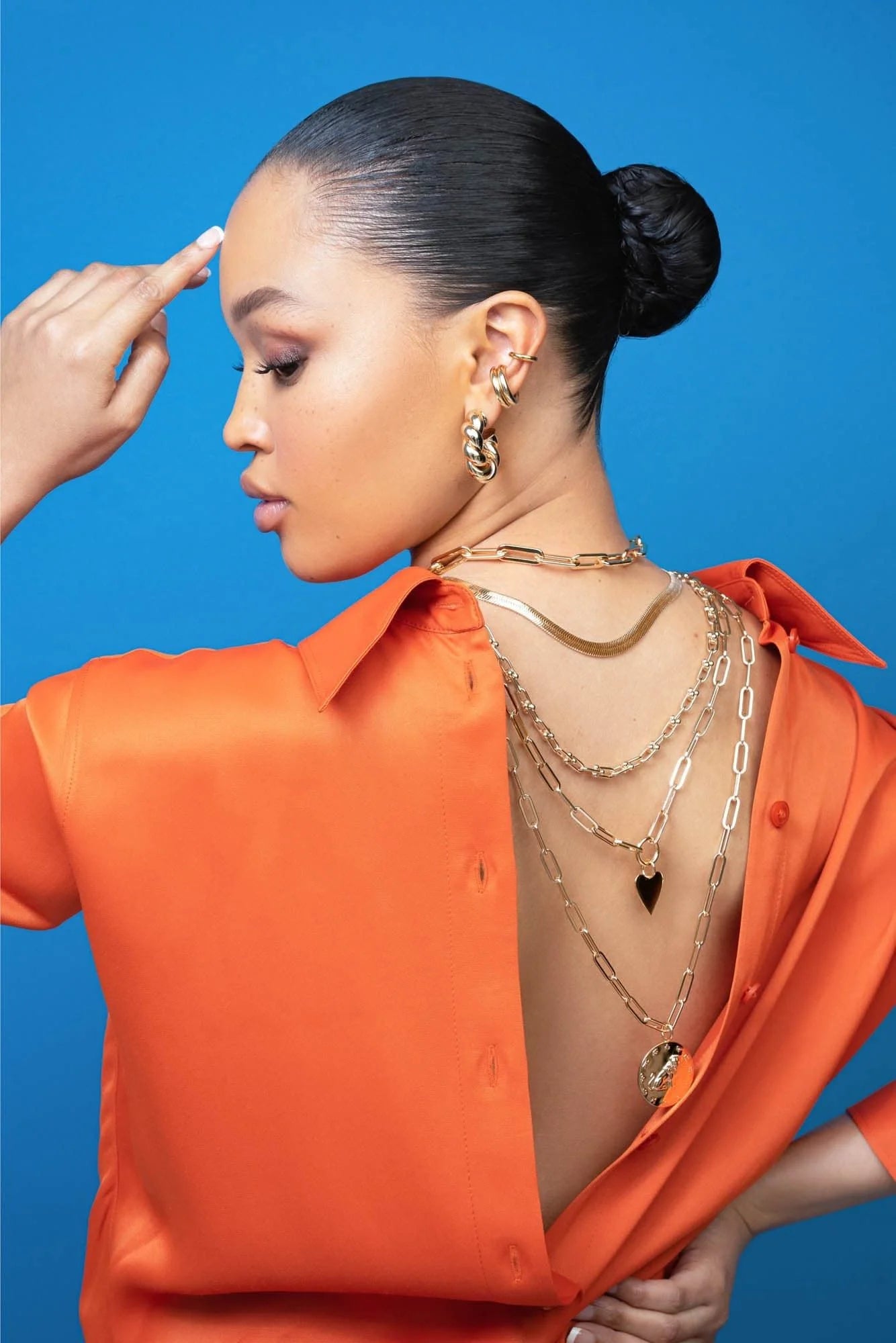 Woman wearing layered gold zodiac pendant Aries Enjoys Stop Aries necklace with orange shirt